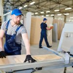 Deux menuisiers équipés découpent des panneaux de bois dans un grand atelier moderne, illustrant le succès d'une création entreprise dans l'artisanat