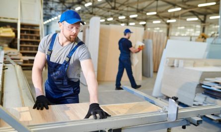 Deux menuisiers équipés découpent des panneaux de bois dans un grand atelier moderne, illustrant le succès d'une création entreprise dans l'artisanat